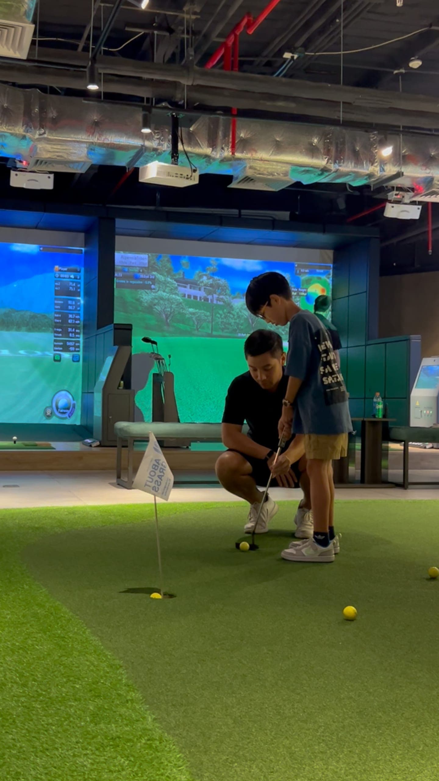 A coach crouches beside a boy on the putting green at LENGOLF